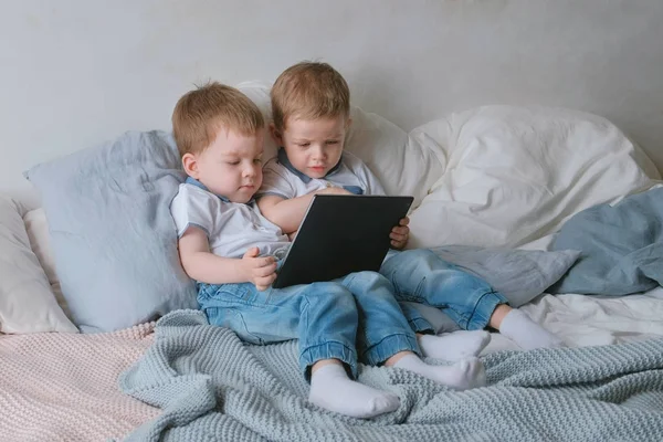 Niños con tableta. Dos niños gemelos niños pequeños mirando dibujos animados en la tableta acostado en la cama . — Foto de Stock