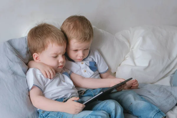 Kids with tablet. Two boys twins toddlers looking cartoon at tablet lying on the bed.