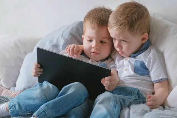 Дети с планшетом. Два мальчика близнецы малыши смотрят мультфильм на планшет, лежащий на кровати . — стоковое фото