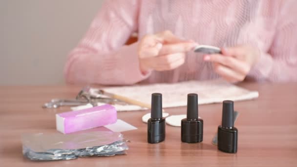 Woman polishes her nails with nail file before remove shellac. Close-up hands. Focus on bottles of shellac. — Stock Video