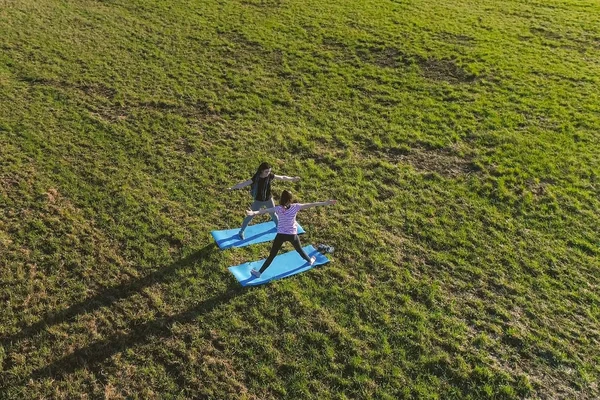 Dos chicas estirándose sobre esteras en el campo. Vista panorámica aérea. Hacer exersices de yoga . —  Fotos de Stock