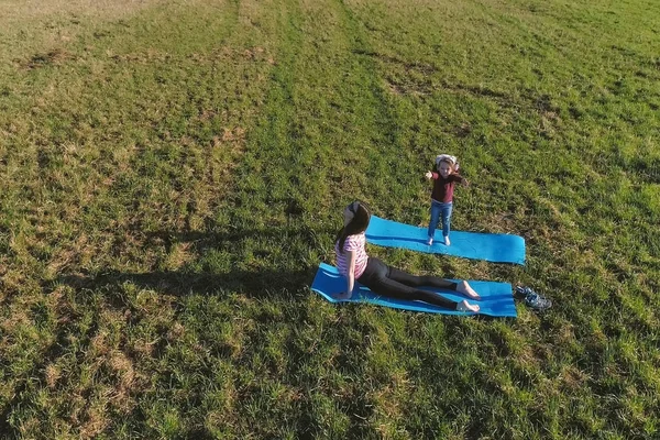 Мама со своей маленькой дочерью растягивается на коврике на поле в теплый летний день. Вид с воздуха . — стоковое фото