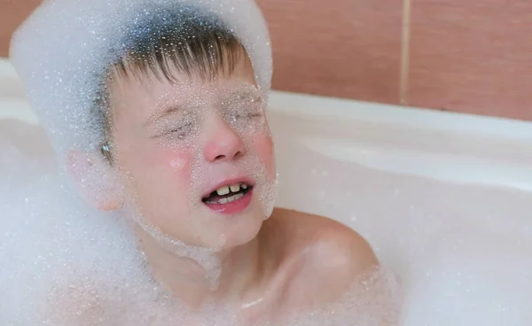 Chłopiec 6-7 lat, przygotuj się na płyn do kąpieli, oczy zamknięte. — Zdjęcie stockowe