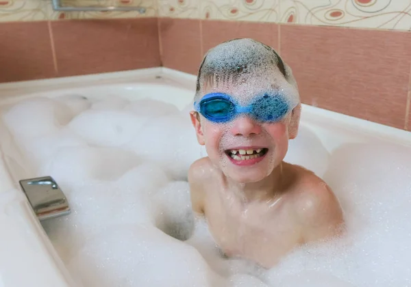 Jongen 6-7 jaar in het schuim en de bril voor het zwembad zitten in de badkamer en glimlachen. — Stockfoto
