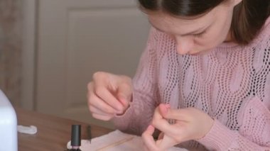 Kadın pembe gomalak ikinci kat tırnaklarını üzerinde koyar ve aşırı manikür için ahşap turuncu stick kullanarak oje temizler.