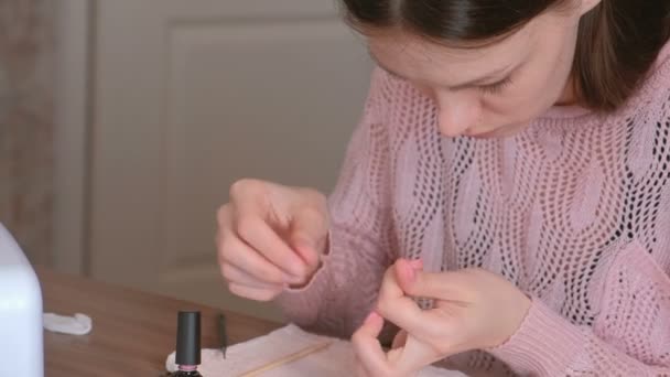 Woman puts second coat of pink shellac on her nails and cleans excess nail Polish using wooden orange stick for manicure. — Stock Video