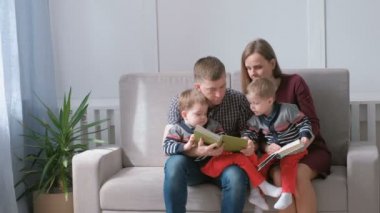 Aile Anne, baba ve iki ikiz kardeşler kanepede oturup kitap okumak. Zaman aile okuma.