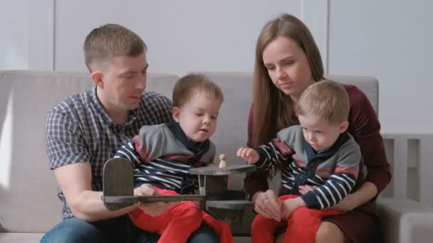 Familie-moeder, vader en twee tweelingbroers spelen samen met houten vliegtuig zittend op de Bank. — Stockvideo