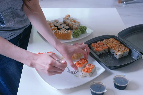 Mujer pone rollos y wasabi de envases de plástico en un plato. Primer plano de las manos . —  Fotos de Stock