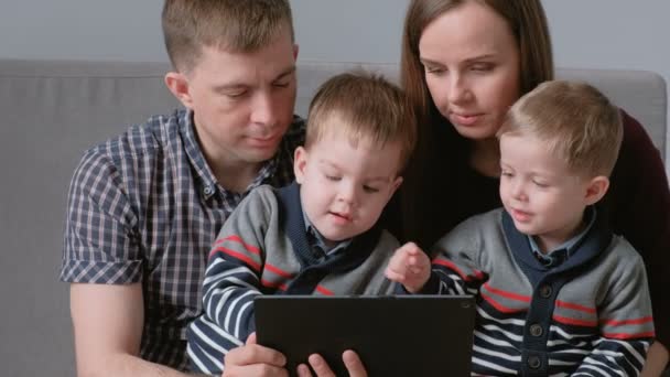 Οικογένεια με το tablet. Μαμά, μπαμπάς και δύο γιους δίδυμα παίζοντας παιχνίδια στο tablet που κάθεται στον καναπέ. — Αρχείο Βίντεο