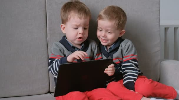 Due fratelli gemelli bambini che giocano insieme giochi su tablet seduti sul divano . — Video Stock