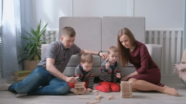 Rodzina Mama, Tata i dwóch braci bliźniaków grać razem budynek z drewnianych klocków na podłodze. — Wideo stockowe