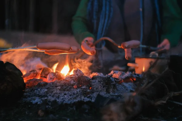 People fry sausages on a fire in the woods at night. Close-up hands. — Stock Photo, Image