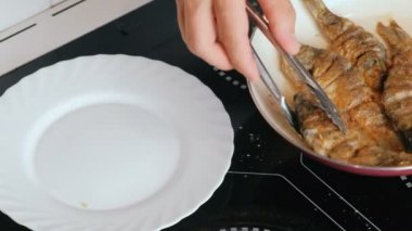Adam tavaya sazan balığı koyuyor. Mutfak maşasıyla yakın plan erkek eli..
