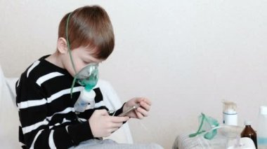 Nebulizatör ve astım tedavisi için kullanın. İnhaler maskesi teneffüs edilmesi ve onun hareket eden telefon içinde oyun oynayan çocuk. Yan görünüm.