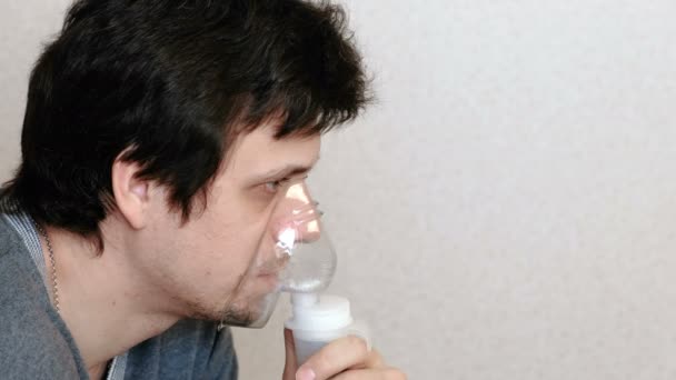 Use nebulizador e inalador para o tratamento. Homem jovem inalando através da máscara do inalador. Vista lateral . — Vídeo de Stock