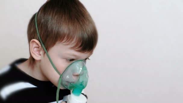 W leczeniu za pomocą rozpylacza i inhalator. Chłopiec wdechu przez inhalator maski. Widok z boku. — Wideo stockowe