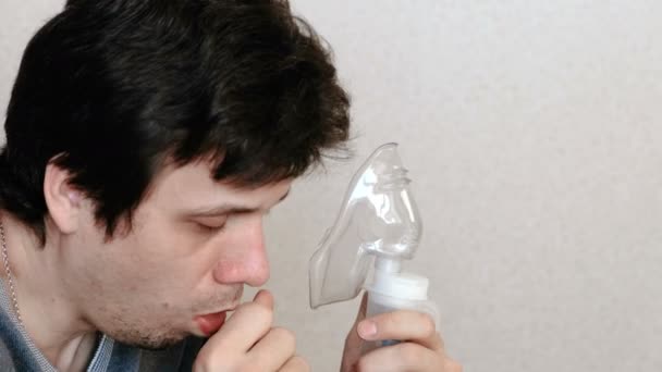 Use nebulizador e inhalador para el tratamiento. Hombre joven inhalando a través de la máscara del inhalador y la tos. Vista lateral . — Vídeos de Stock