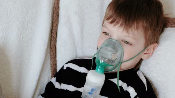 Uso de nebulizador e inhalador para el tratamiento. Niño inhalando a través de la máscara del inhalador acostado en el sofá . — Vídeos de Stock