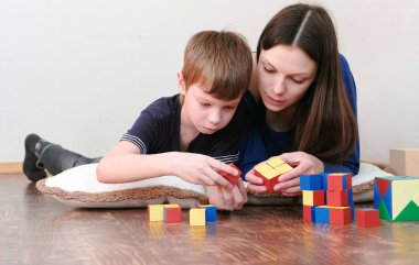 Anne ve oğlu birlikte ahşap renkli eğitim oynayan yerde yatarken blok oyuncak.