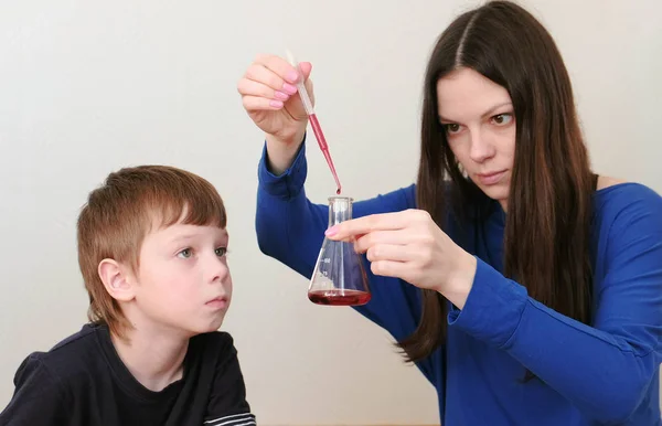 Moeder en zoon doen een chemische ervaring met het pipet, de kolf en de rode vloeistof. — Stockfoto