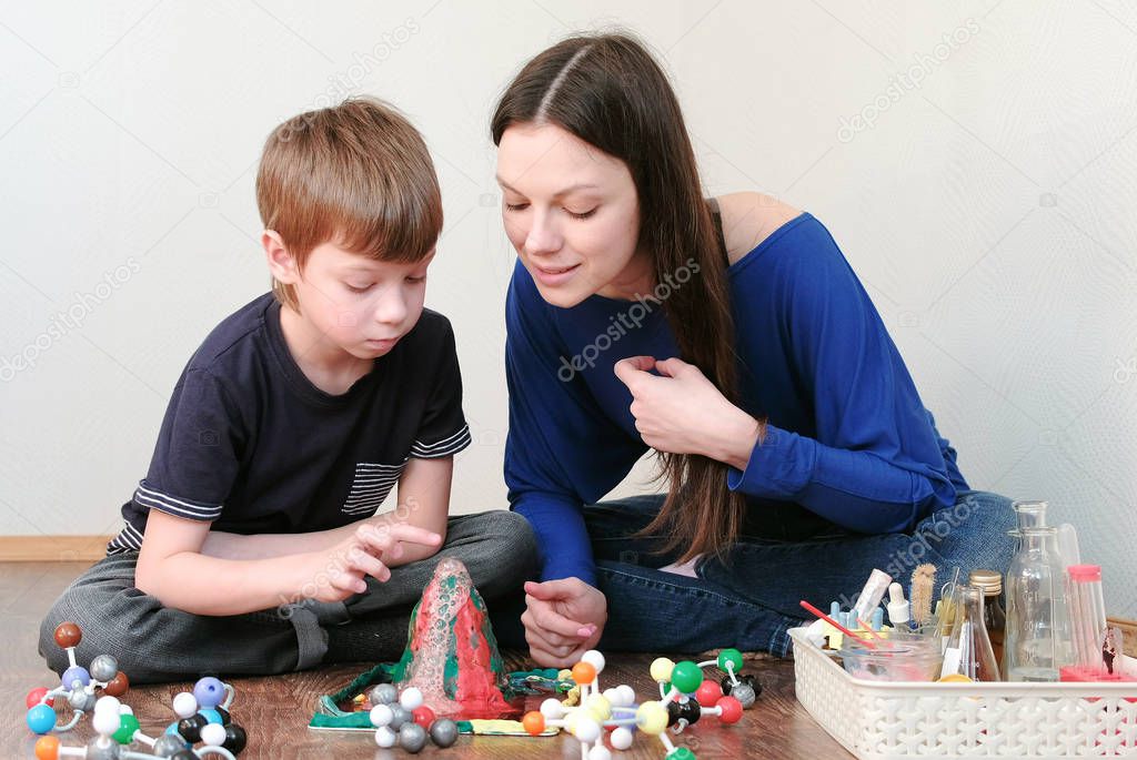 Mom and son looking at chemical reaction with gas emission. Experience with plasticine volcano at home.