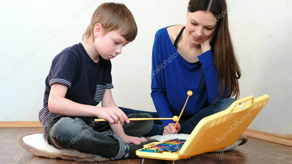 Playing music instrument. Teacher teaches the boy to play the xylophone
