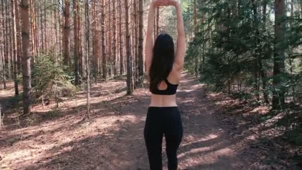 A mulher de fato desportivo vai para o parque e aquece antes do Jogging. Vista traseira. Movimento lento . — Vídeo de Stock