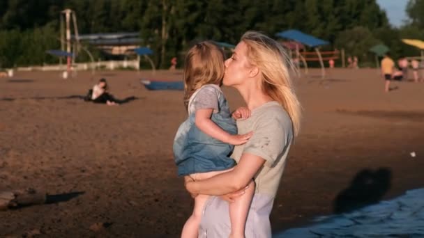 Dziewczynka w ramionach matki pokazuje coś z jej rękę w bok na plaży nad rzeką. — Wideo stockowe