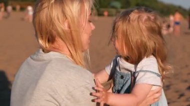 Güzel sarışın anne ve kızı gün batımında sahilde sarılma.