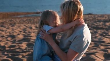 Güzel sarışın anne ve kızı gün batımında sahilde sarılma.