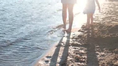 Güzel sarışın anne ve kızı gün batımında sahilde yürümek. Yakın çekim bacaklar
