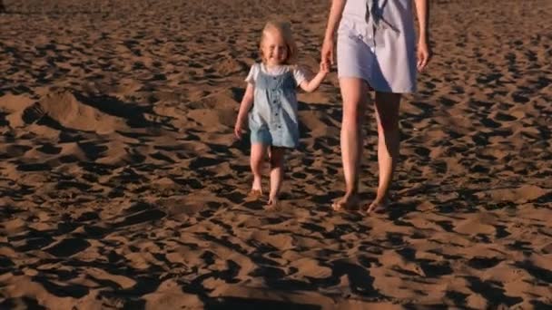 美しい金髪ママと娘は、日没でビーチを散歩します。. — ストック動画