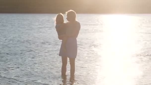 Beautiful blonde mother and daughter walk along the river on the water at sunset. — Stock Video