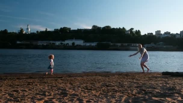 Hermosa mamá rubia e hija corren una hacia la otra en el río Banco al atardecer . — Vídeo de stock