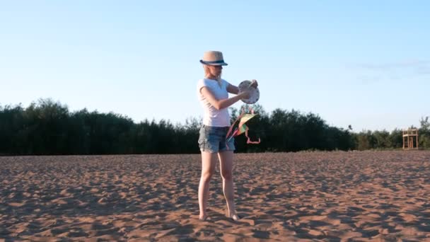 Mooie blonde in een hoed lanceert een vlieger op het strand. — Stockvideo