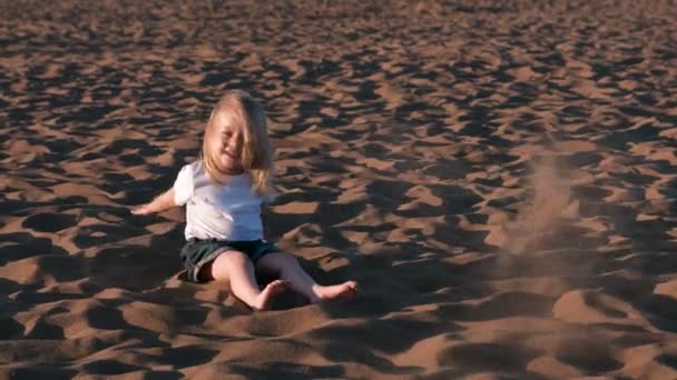 Hermosa niña feliz rubia jugando y lanzando arena en la playa . — Vídeos de Stock