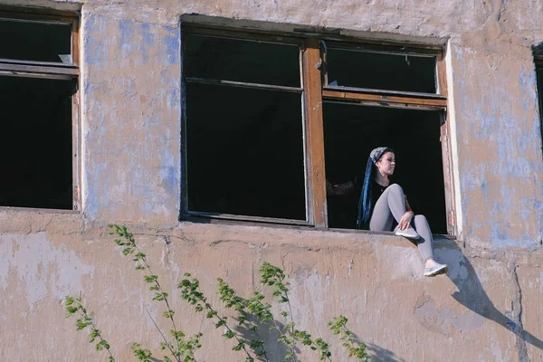 Женщина сидит на окне разрушенного многоэтажного здания со многими разбитыми окнами . — стоковое фото