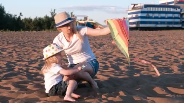 Hermosa rubia en un sombrero mamá e hija lanza una cometa en la playa . — Vídeo de stock