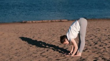 Şehrin nehir kenarında kumsalda yoga yaparken kadın. Padangustasana güzel görünümünde poz.