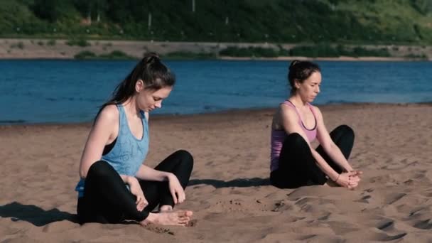 Zwei Frauen beim Yoga am Strand am Fluss in der Stadt. Schöne Aussicht in der Stadt. Individuelles Training. — Stockvideo