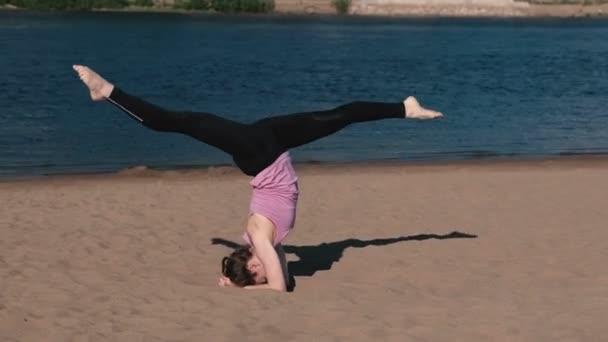 Mujer haciendo yoga en la playa junto al río en la ciudad. Hermosa vista. Soporte de mano. Twine en el aire. Alta velocidad . — Vídeos de Stock