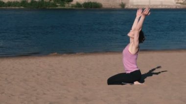 Şehrin nehir kenarında kumsalda Yoga esneme kadın. Güzel bir şehir manzarası. Nefes egzersizi.