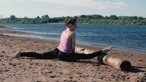 Kvinnan gör stretching sitter på garn i sandstranden vid solnedgången. — Stockvideo