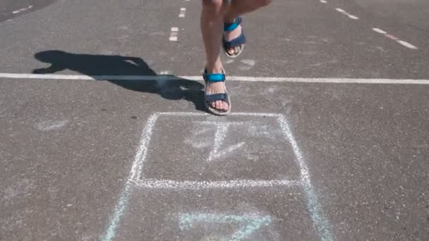 Jongen springt spelen Hinkelspel in de straat. Close-up benen. — Stockvideo