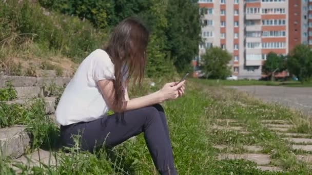 Vrouw typt een bericht op telefoon zitten in park. — Stockvideo