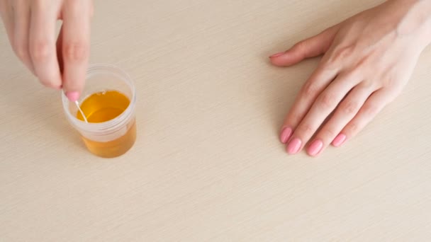A mulher faz um teste de gravidez. Mergulha a tira de teste em um copo de urina. Mãos fechadas . — Vídeo de Stock