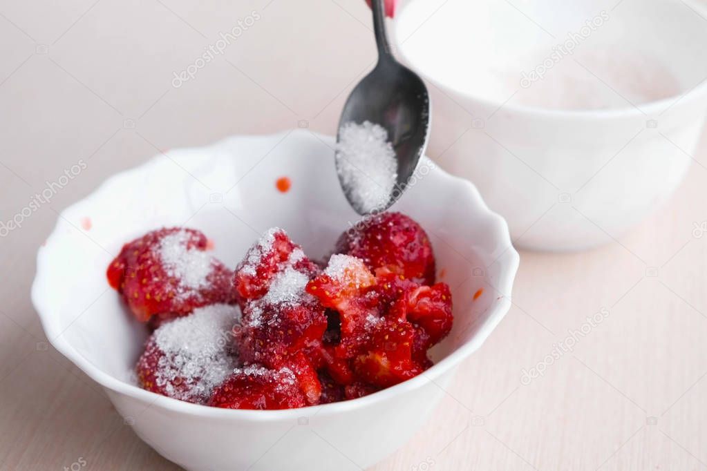 Woman kneads strawberries with a spoon and mixes it with sugar, making jam. Close-up hand.