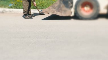 Kent içi temizlik. Adam bir kürekle kir toplar ve her şeyi Ekskavatör kova içine atar. Bacaklar yakın çekim.
