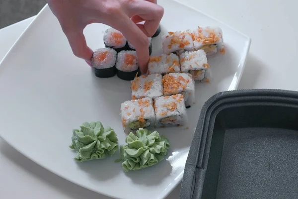 Mujer pone rollos y wasabi de envases de plástico en un plato. Primer plano de las manos . —  Fotos de Stock